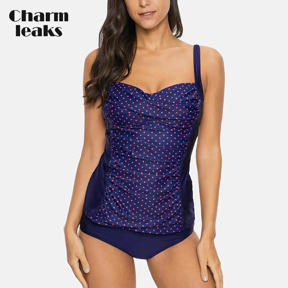 Woman wearing a navy blue polka dot swimsuit with 'Charm leaks' branding.