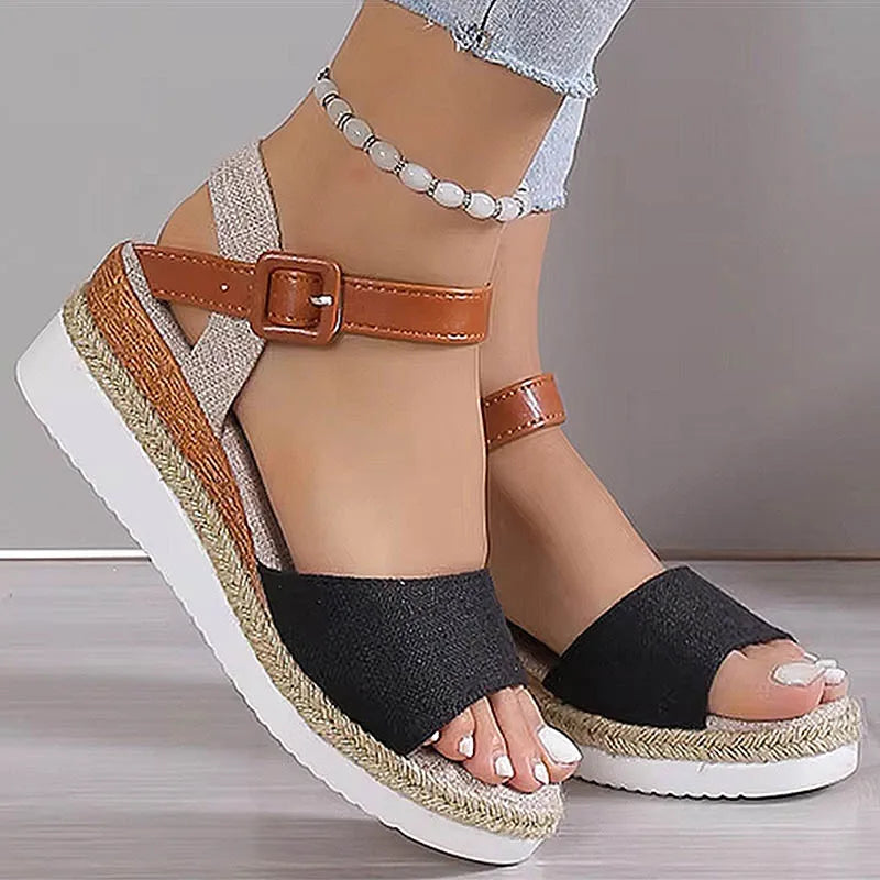 Black wedge sandals with brown straps worn by a person on a neutral background