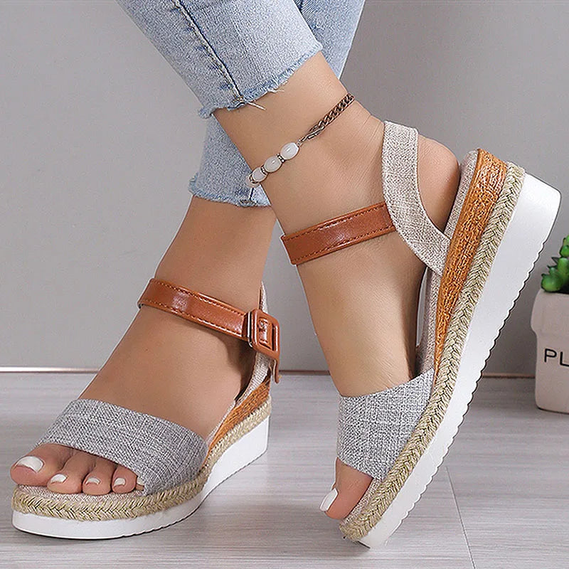 Gray sandals with brown straps worn by a person on a light wooden floor.