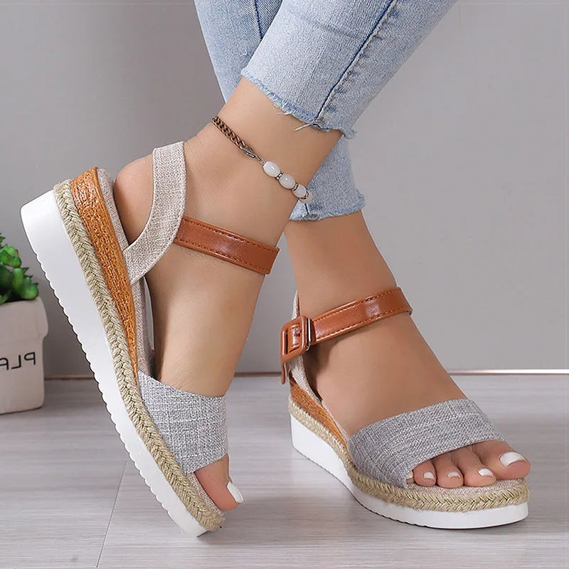 Gray wedge sandals with brown straps worn by a person on a light wooden floor.