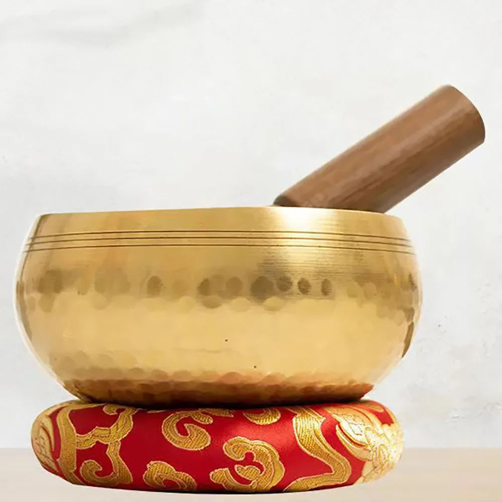 Gold singing bowl with wooden striker on a white background