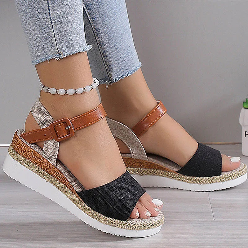 Black wedge sandals with brown straps worn by a person on a neutral background