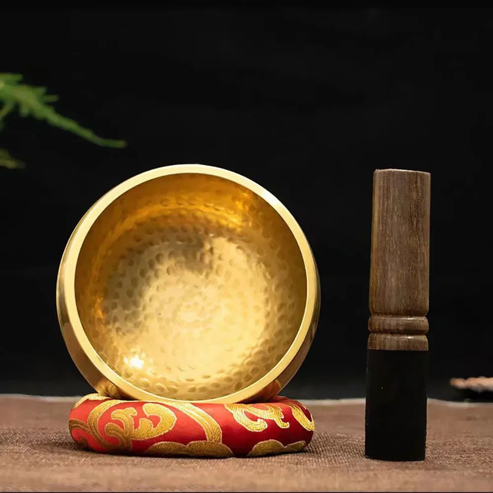 Gold singing bowl with a wooden striker on a dark background