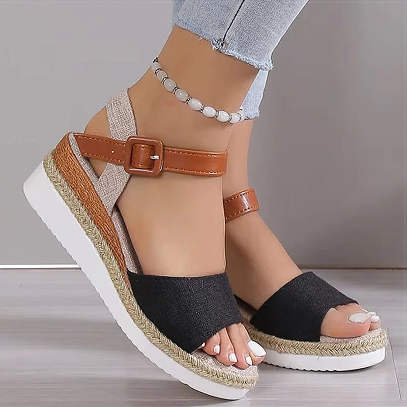 Black wedge sandals with brown straps worn by a person on a neutral background