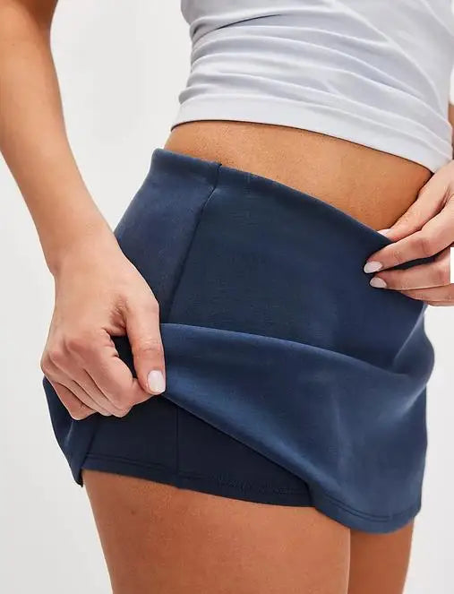 Person wearing a navy blue skirt with a white top on a light gray background